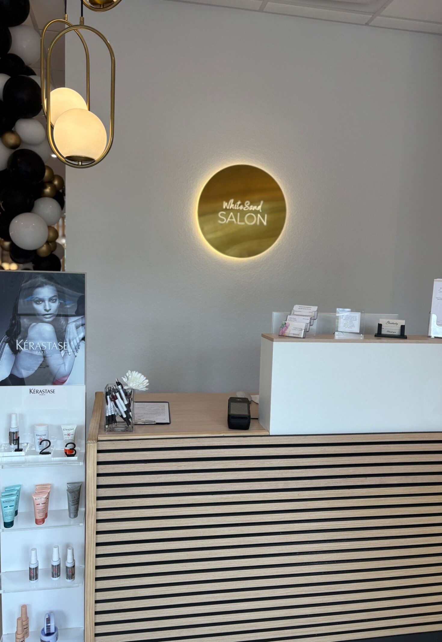 The White Sand Salon front desk in Clearwater, with the backlit gold logo sign above the slatted reception counter
